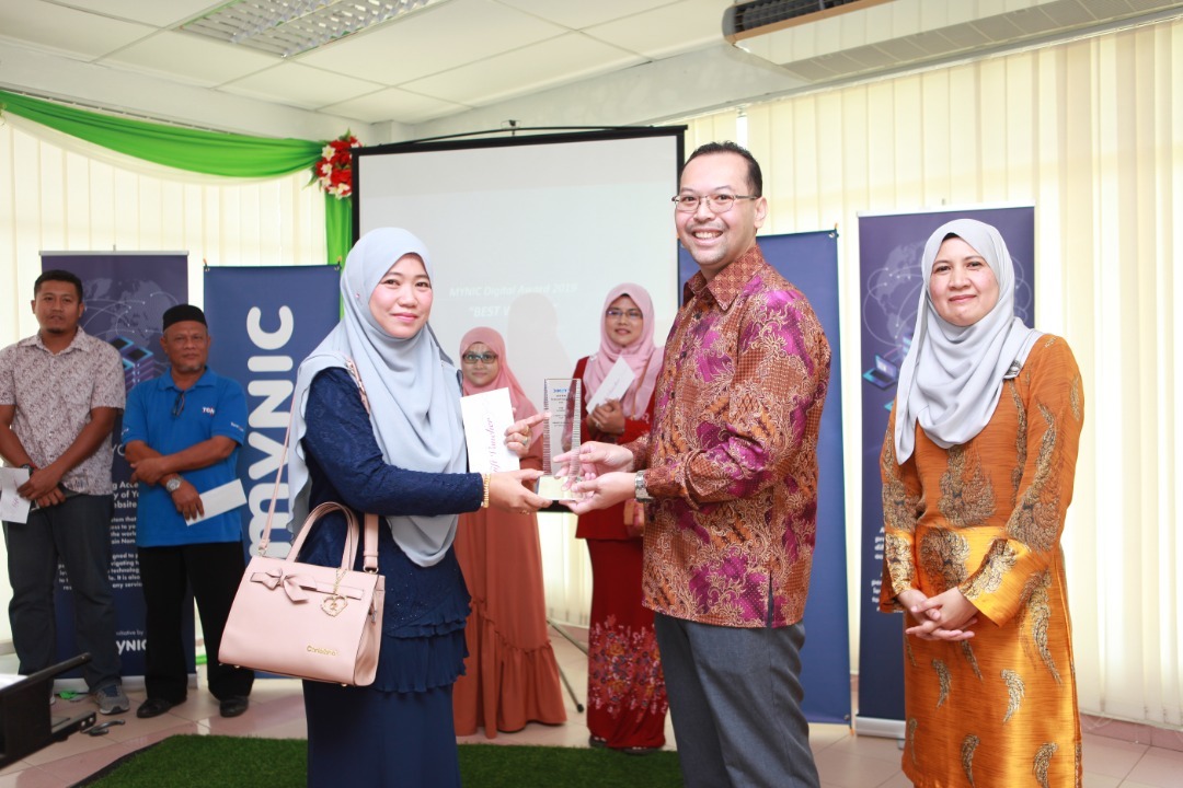 Datuk Ts. Hasnul menyerahkan trofi MYNIC Digital Award 2019 kepada Rosliza atas pencapaianya dalam Program Latihan Penguasaan Pasaran Digital.